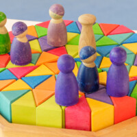Bunte Holzbausteine in Dreieckform und verschiedenen Farben, auf denen kleine Holzfiguren stehen; pädagogisches Spielmaterial auf hellem Tisch.